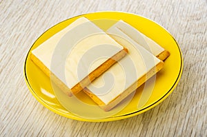 Crackers with slices of melted cheese in saucer on wooden table