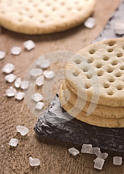 Crackers stack together on black stone, coarse sugar on wooden b