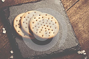 Crackers stack together on black stone, coarse sugar on wooden b