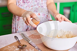 Cracking an egg to a flour. Close-up of woman`s hands breaks an egg for pastry