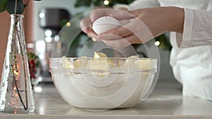 Cracking fresh egg into a bowl with flour and sugar to prepare dough for baking Christmas cookies