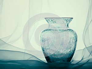 Crackle glass vase with net curtain, still life.