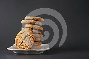 A crackly gingerbread cookie leans against a stack of cookies on a white plate with black background