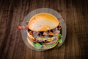 Craft beef burger with cheese, bacon, caramelized onion and rocket leafs on wood table and rustic background