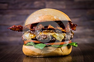 Craft beef burger with cheese, bacon, caramelized onion and rocket leafs on wood table and rustic background