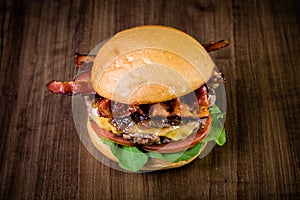 Craft beef burger with cheese, bacon, caramelized onion and rocket leafs on wood table and rustic background