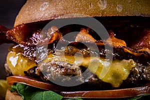 Craft beef burger with cheese, bacon, caramelized onion and rocket leafs on wood table and rustic background
