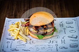 Craft beef burger with cheese, bacon, rocket leafs, caramelize onion and french fries on wood table and rustic background