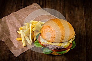 Craft beef burger with cheese, rocket leafs and french fries on wood table and rustic background