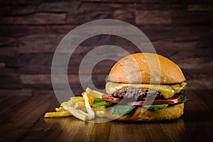 Craft beef burger with cheese, rocket leafs and french fries on wood table and rustic background