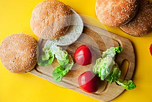 Craft beef burgers on round wooden cutting board with vegetables. Flat lay on black textured background