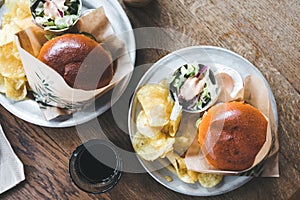 Craft beef burgers with vegetables on a plate with chips and salad on a wooden table.