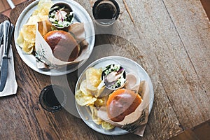 Craft beef burgers with vegetables on a plate with chips and salad on a wooden table.