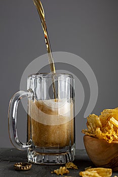 Craft beer is being poured into a glass mug with handle in a pub with dark background
