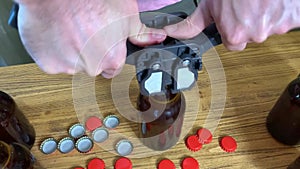 Craft beer brewing at home, man`s hands closes brown glass beer bottles with plastic capper on wooden table with red crown caps.