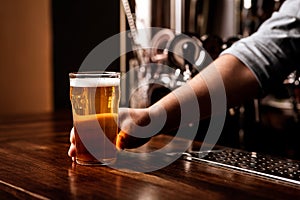 Craft beer for regular client. Bartender gives glass of light lager in interior of pub