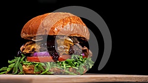 Craft burger is cooking on black background. Consist: sauce, arugula, tomato, onion, bacon, currant sauce, ricotta