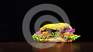 Craft burger is cooking on black background. Consist: sauce, lettuce, tomato, red onion, pickle, cheese, bacon, air bun