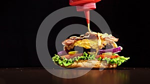 Craft burger is cooking on black background. Consist: sauce, lettuce, tomato, red onion, pickle, cheese, bacon, air bun