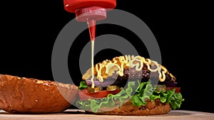 Craft burger is cooking on black background. Consist: sauce, lettuce, tomato, red onion, pickle, cheese, bacon, air bun