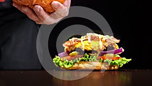 Craft burger is cooking on black background. Consist: sauce, lettuce, tomato, red onion, pickle, cheese, bacon, air bun