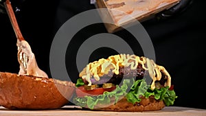 Craft burger is cooking on black background. Consist: sauce, lettuce, tomato, red onion, pickle, cheese, bacon, air bun