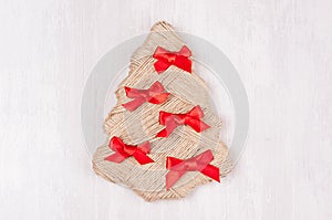 Craft christmas tree of twine with red bows on white wood table with copy space.