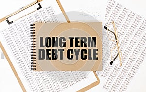 Craft colour notepad with text LONG TERM DEBT CYCLE. Notepad with eyeglasses and text documents. Business concept