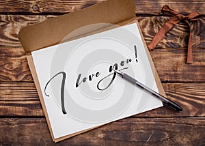 Craft envelop, white paper with sign `I love you` and black pen on old brown wooden  table