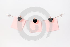 Craft hearts wooden black chalkboard clothespins on rope twine on white wall with pink paper note, horizontal. Garland decoration