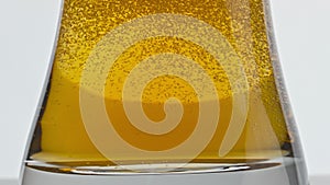 Craft iced beer fizzing glass bottom closeup. Pasteurized barley lager bubbling