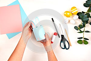 Craft making process. Female hands hold a glass for pencils on a light wooden table. Step by step. View from above. Children`s