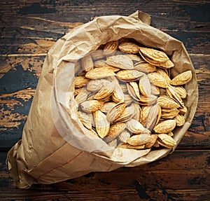 Craft paper bag with roasted almonds on a dark brown wooden background, close up, top view