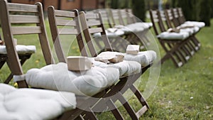 Craft paper bags lie on folding wooden chairs with cushions on lawn.