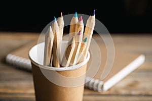 Craft paper coffee cup, pencils and recycled notebook on wooden background.