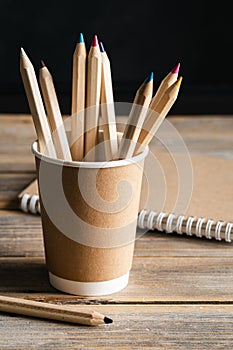 Craft paper coffee cup, pencils and recycled notebook on wooden background.