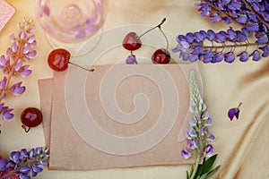 Craft paper mock up. Lupins purple flowers, wine glass, apple and cherry decorations. Summer invitation, birthday