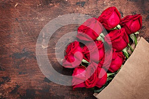 Craft paper shopping bag with flowers on wooden background. Red roses in a brown kraft bag. Copy space