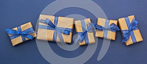 Craft paper wrapped gift boxes in a row on blue background, flat lay with copy space. Christmas abstract banner