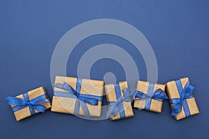 Craft paper wrapped gift boxes in a row on blue background, flat lay with copy space. Christmas abstract mock up