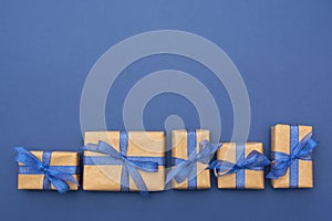 Craft paper wrapped gift boxes in a row on blue background, flat lay with copy space. Christmas abstract mock up