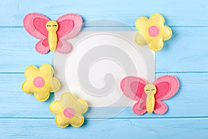 Craft pink and yellow butterfly and flowers with white paper, copyspace on blue wooden background. Hand made felt toys. Abstract s