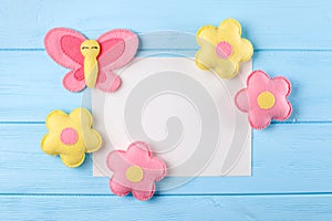 Craft pink and yellow butterfly and flowers with white paper, copyspace on blue wooden background. Hand made felt toys. Abstract s