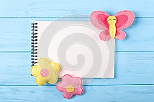 Craft pink and yellow butterfly and flowers with white paper, copyspace on blue wooden background. Hand made felt toys. Abstract s