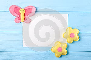 Craft pink and yellow butterfly and flowers with white paper, copyspace on blue wooden background. Hand made felt toys. Abstract s