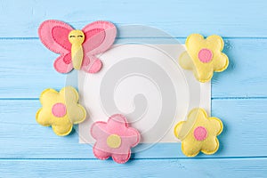 Craft pink and yellow butterfly and flowers with white paper, copyspace on blue wooden background. Hand made felt toys. Abstract s