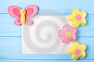 Craft pink and yellow butterfly and flowers with white paper, copyspace on blue wooden background. Hand made felt toys. Abstract s