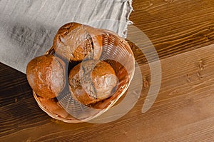 Craft three bread buns in a wicker basket, on a wooden cutting board. Simple breakfast on wooden background. copy space.