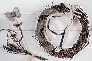 Crafting DIY hanging woven willow wreath of wickers with tape bow composition. White wood background. Traditional decor