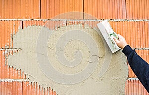 Craftperson plastering brick wall with trowel, construction industry background